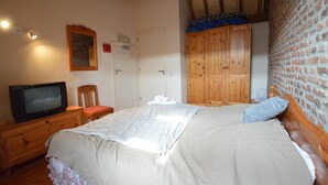 Un dormitorio con cama, televisor, armario de madera y pared de ladrillo.