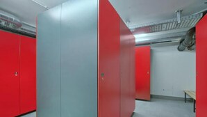 Een kamer met rode lockers en een grijze kast, een bankje en een betegelde vloer.