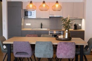 Une cuisine moderne avec une table à manger en bois, quatre chaises et des luminaires suspendus.