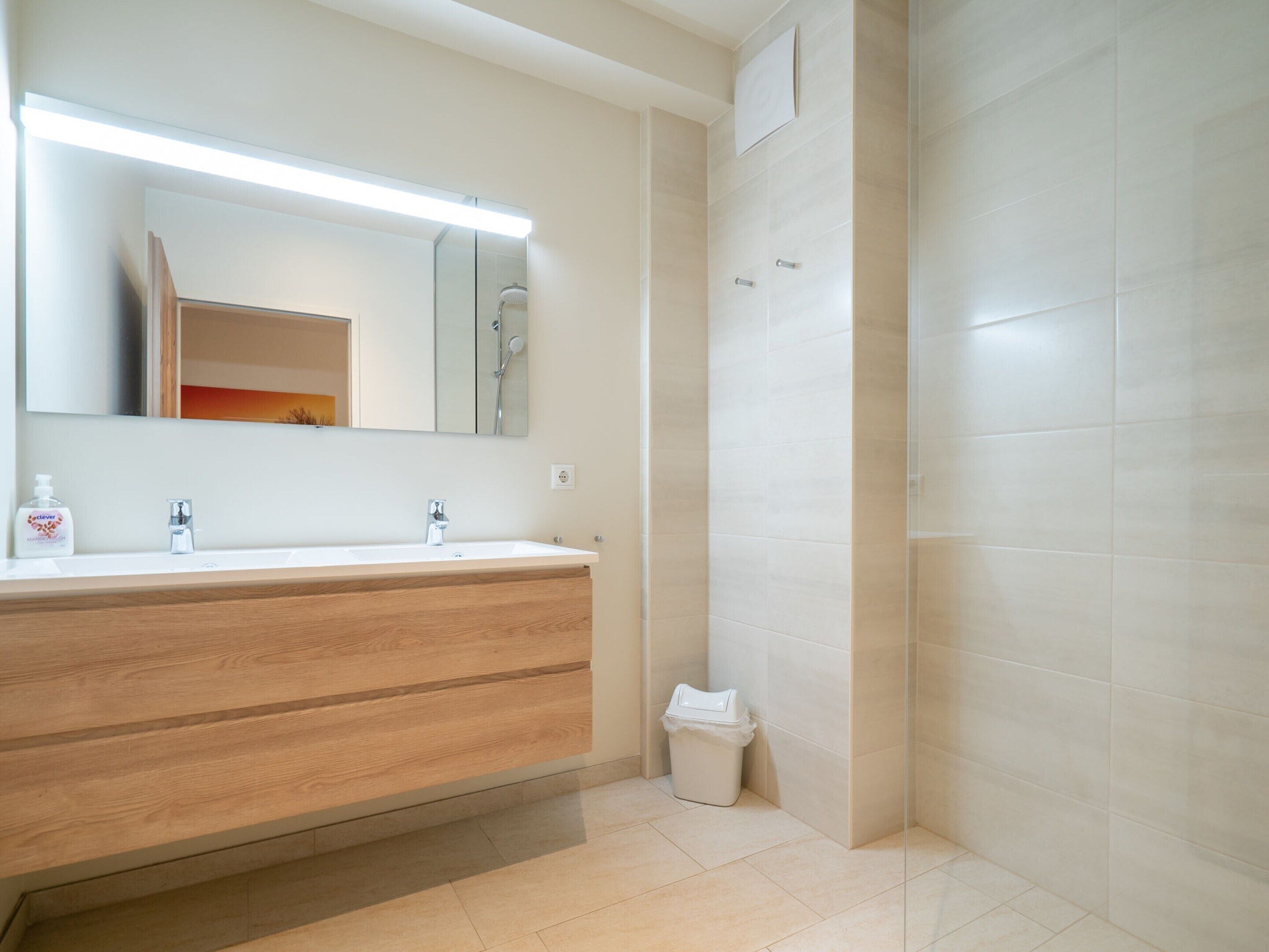 A modern bathroom with a wooden vanity, a large mirror, and a shower area.