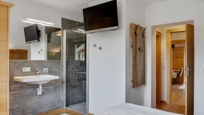 Un dormitorio moderno con una cama grande, ducha integrada, lavamanos y un televisor montado en la pared.