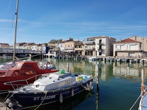 Uma marina com barcos atracados, céu claro e edifícios com varandas.