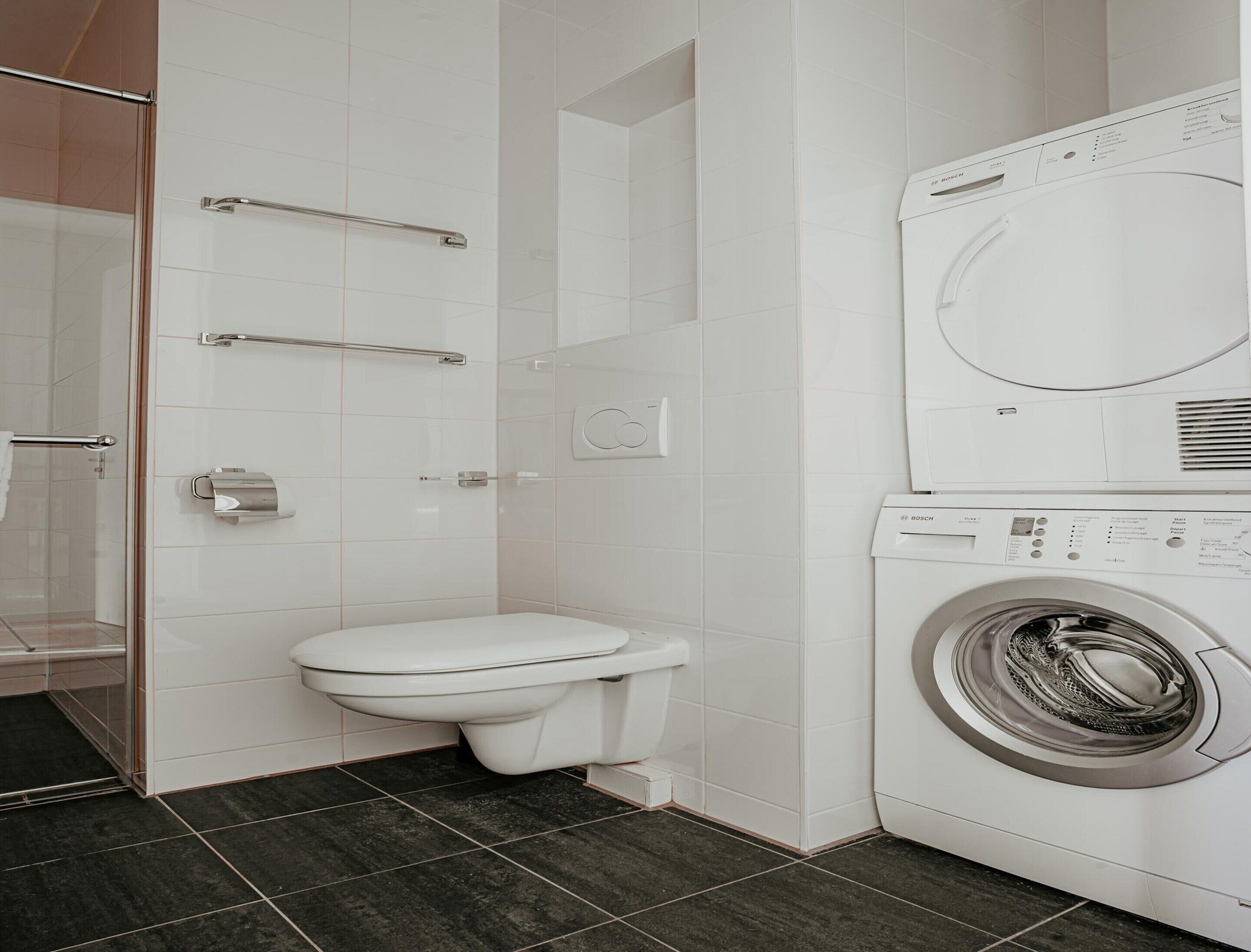 A modern bathroom with a toilet, a glass shower enclosure, and a Bosch washing machine.