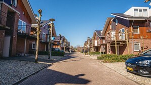 Une rue résidentielle bordée de maisons modernes, avec une chaussée pavée et des voitures garées.
