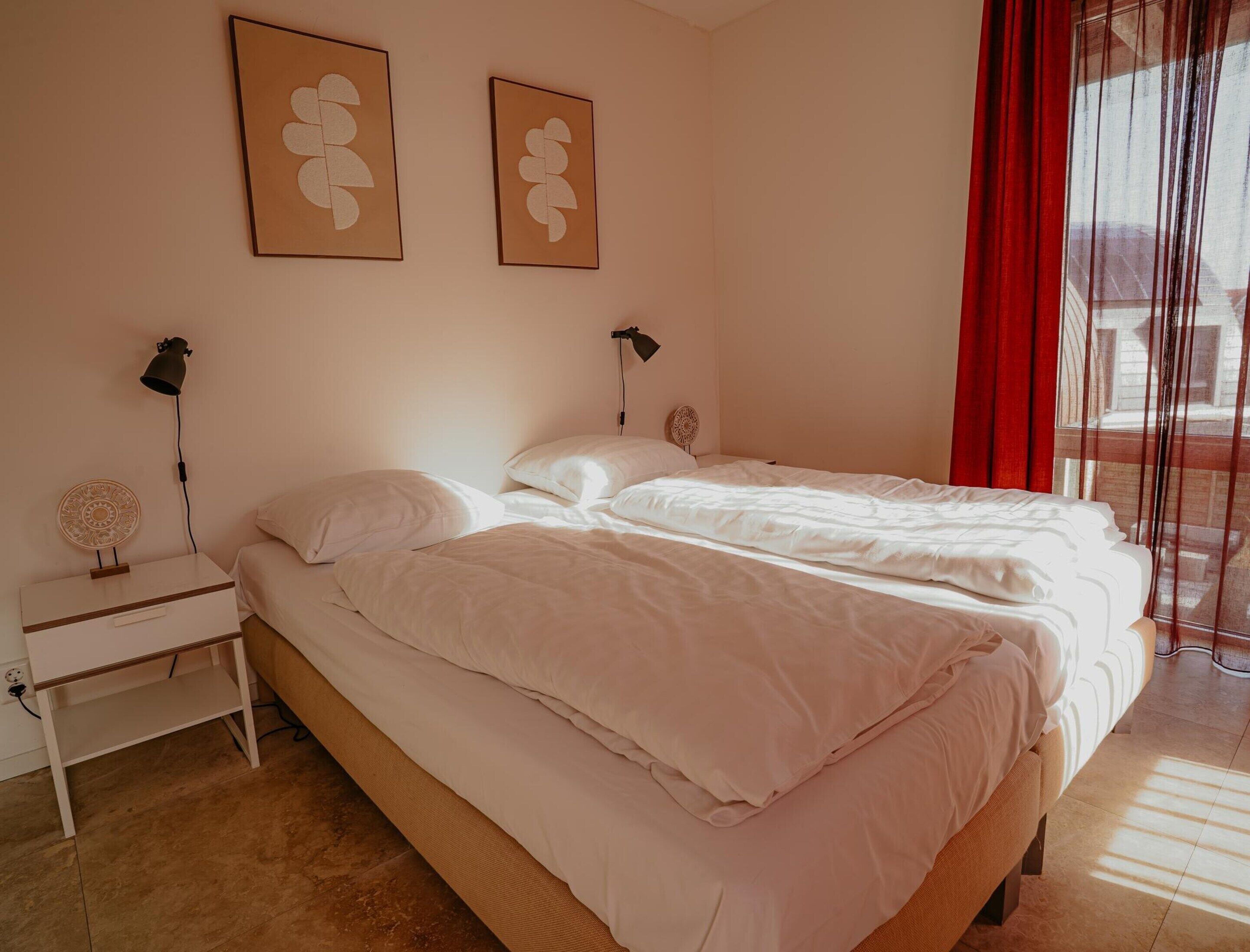 A bedroom with two beds, a bedside table with a lamp, and a wall-mounted fan.