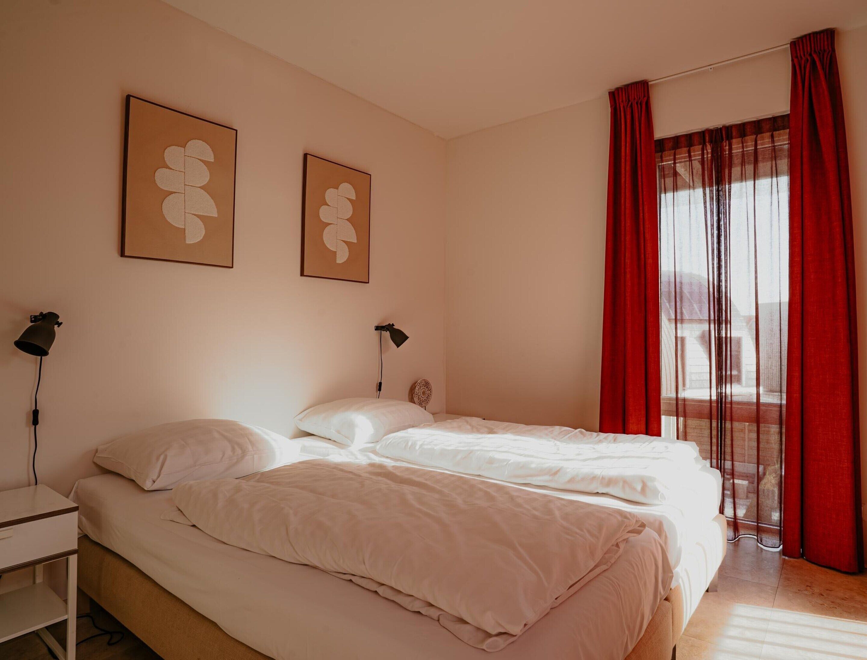 Un dormitorio con dos camas, un escritorio y una ventana con cortinas rojas.