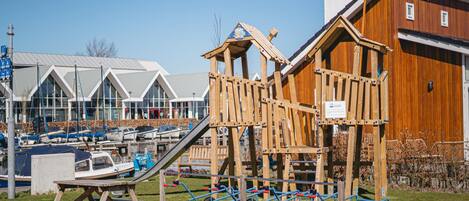 A playground with a slide and a wooden climbing structure, a picnic table, and a boat dock in the background.
