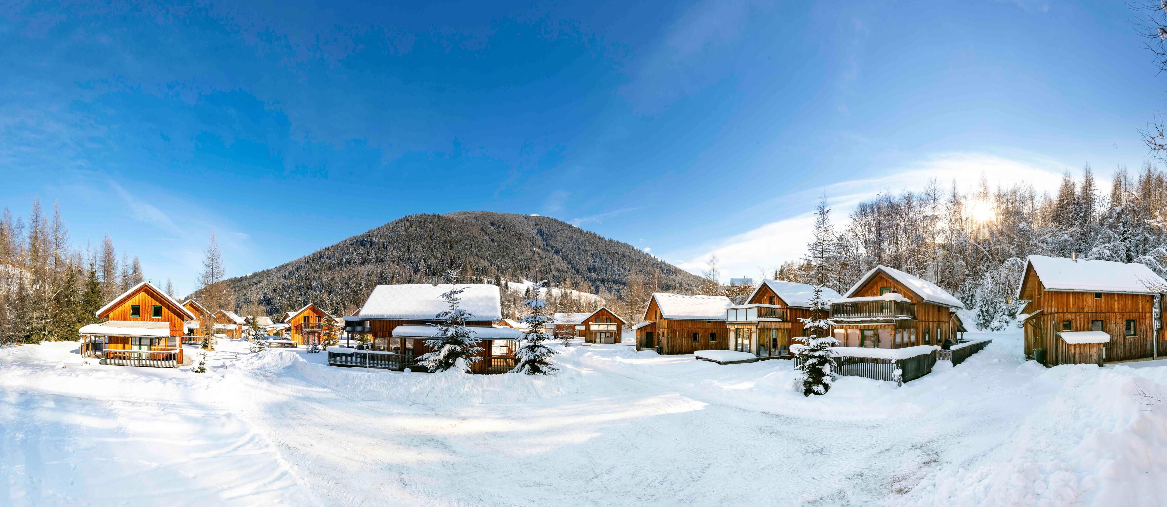 A snow-covered village with wooden cabins and a mountain in the background.