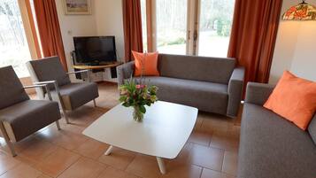 A living room with a grey sofa, two armchairs, a white coffee table, and a TV on a wooden stand.