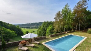 A rectangular pool with lounge chairs and an umbrella, surrounded by a stone wall and trees, overlooking a green landscape. - Retreat Near Siorac-en-perigord (Saint-Germain-de-Belvès)