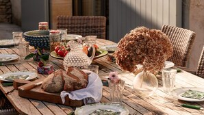 A wooden table set outdoors with plates, glasses, a bread basket, and a decorative vase. - Retreat Near Siorac-en-perigord (Saint-Germain-de-Belvès)