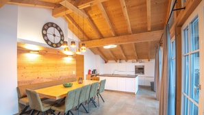 Une cuisine moderne avec des poutres en bois, un coin repas avec une table et des chaises en bois, et une grande fenêtre avec des rideaux.