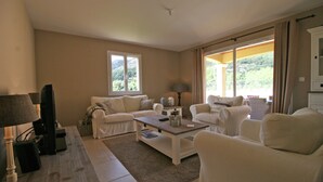 A living room with a sofa, armchairs, a coffee table, a TV, and a lamp. - Contemporary Villa With Pool (Plan-de-la-Tour)