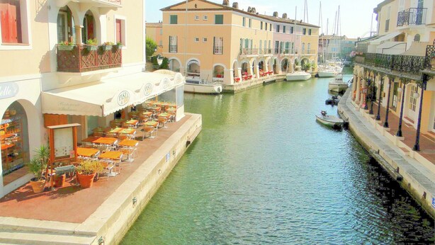 A canal with buildings on either side, outdoor seating, and boats. - Contemporary Villa With Pool (Plan-de-la-Tour)