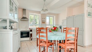 Uma cozinha com armários brancos, uma mesa de jantar com cadeiras de madeira e um pendente.