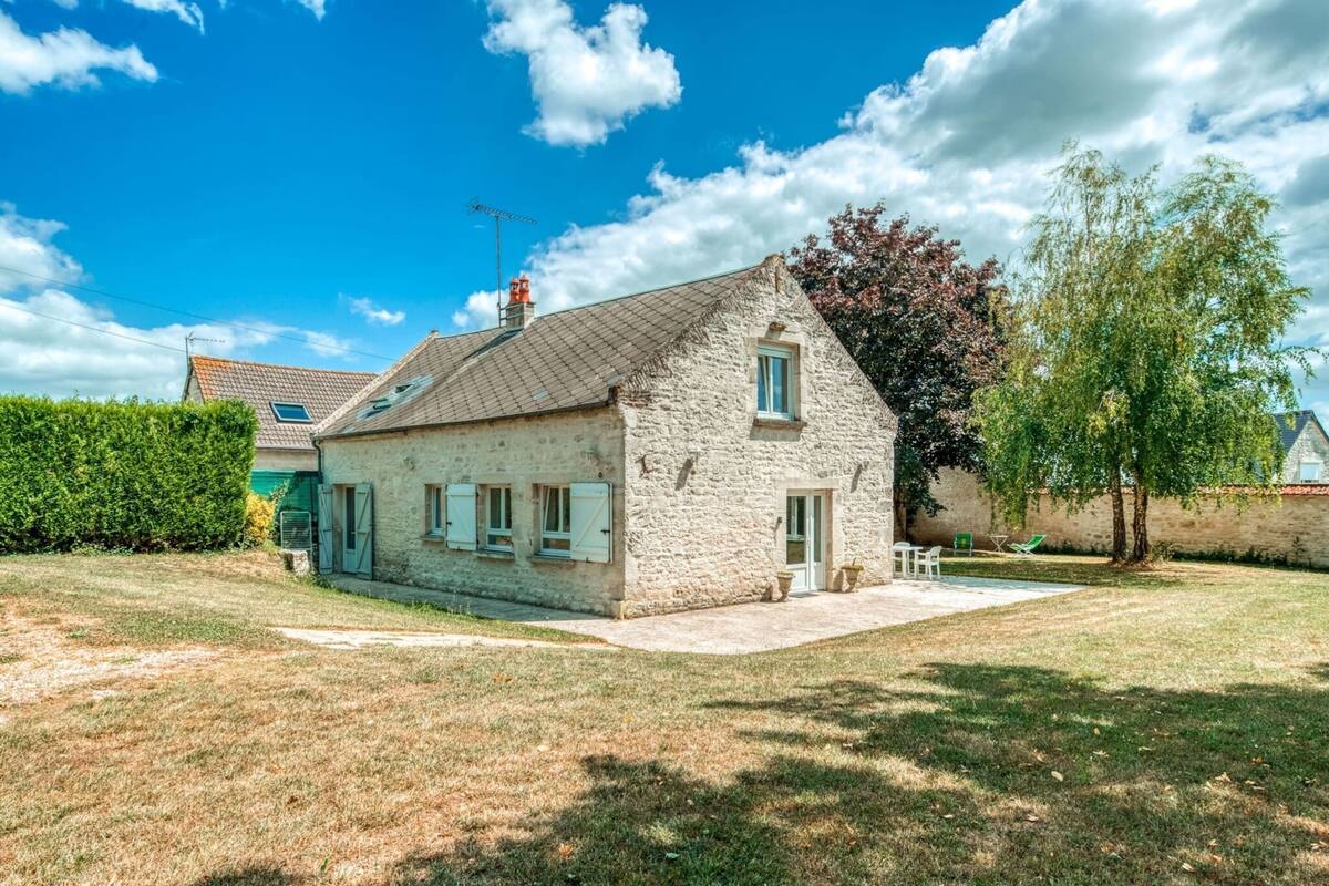 A stone house with a tiled roof, a small front yard, and a tree to the right.
