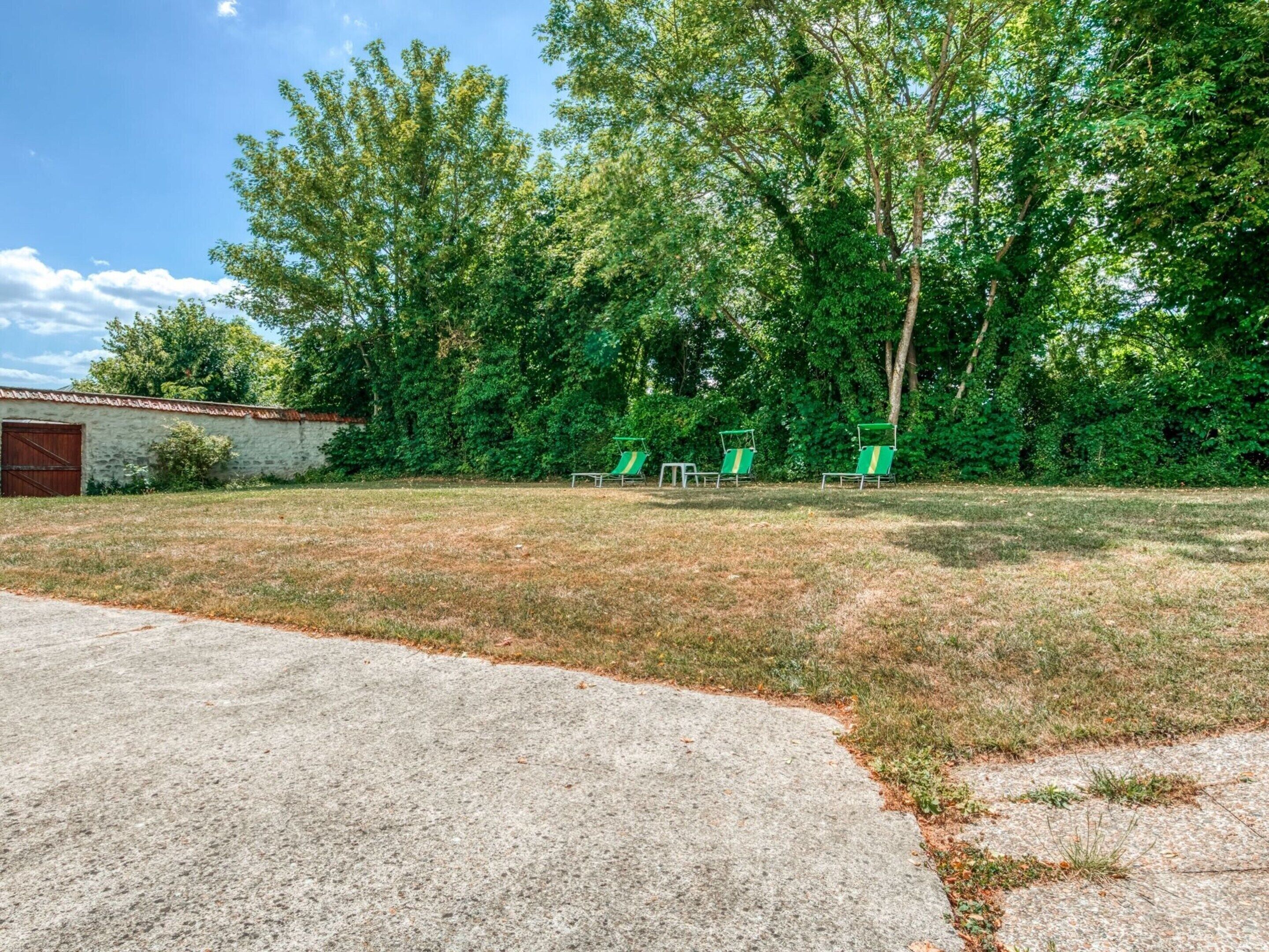 A grassy yard with a paved driveway, a small shed, and three green lawn chairs.
