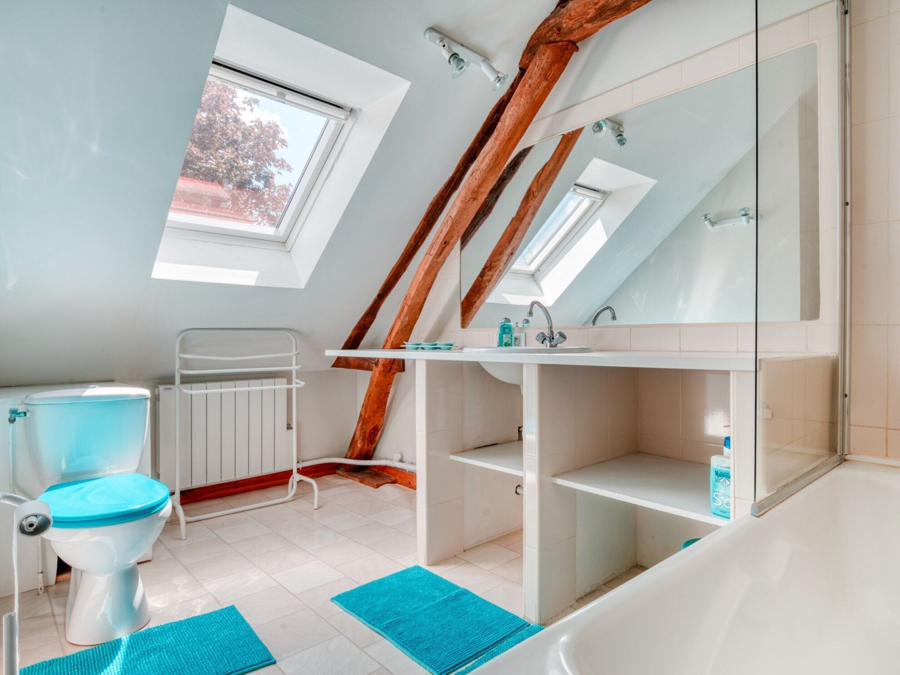 Un baño moderno con tragaluz, inodoro blanco, bañera y un espejo grande.
