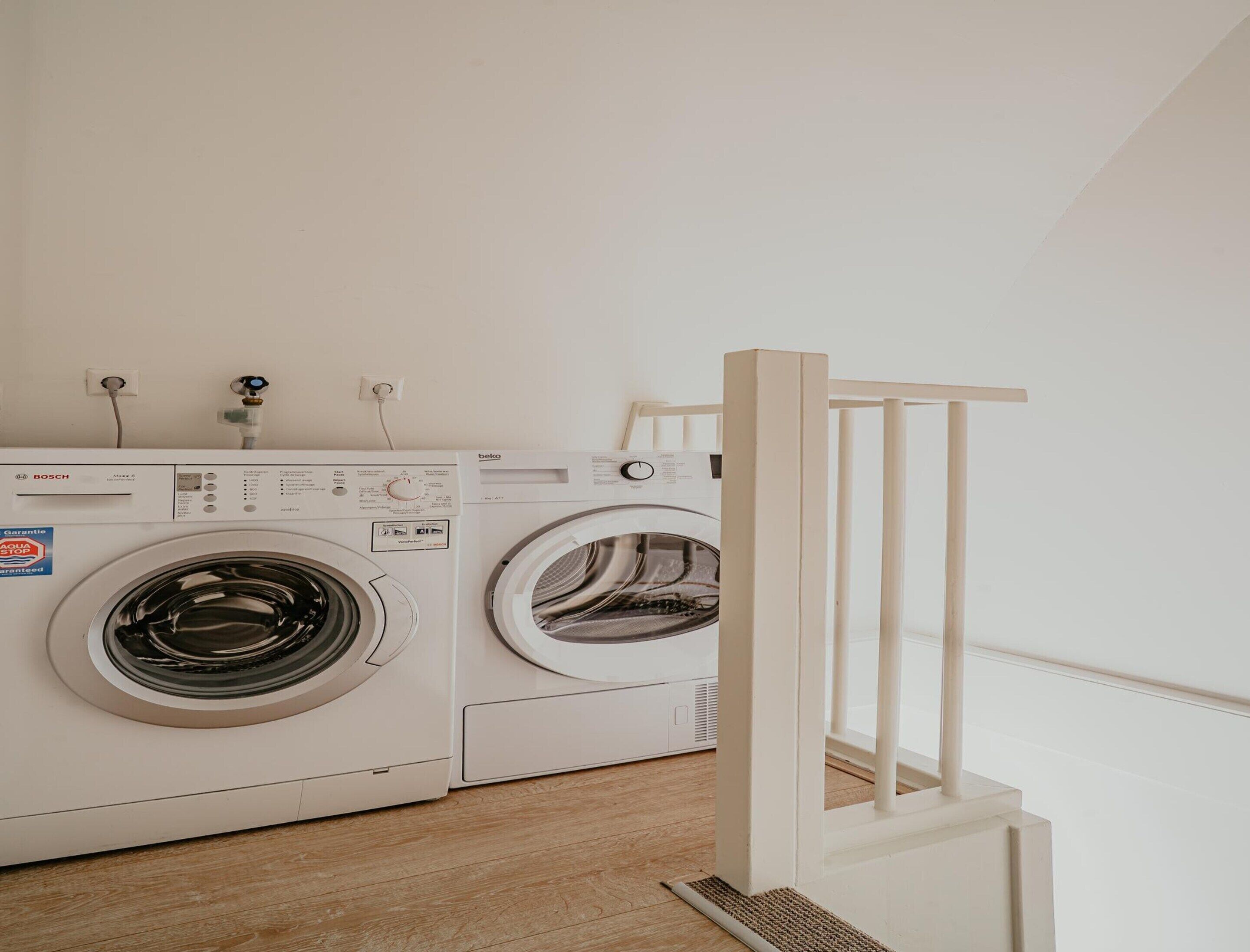 A laundry area with two white Bosch washing machines, a wooden chair, and a white wall.
