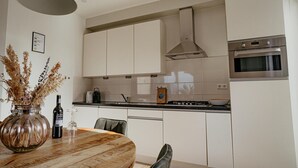 A modern kitchen with white cabinets, a stainless steel oven, and a round wooden dining table. - Luxury Apartment Near the Beach (Egmond aan Zee)