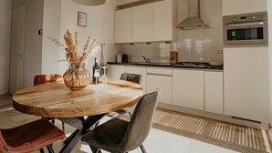 A modern kitchen with white cabinets, a round wooden dining table, and a hanging light fixture. - Luxury Apartment Near the Beach (Egmond aan Zee)