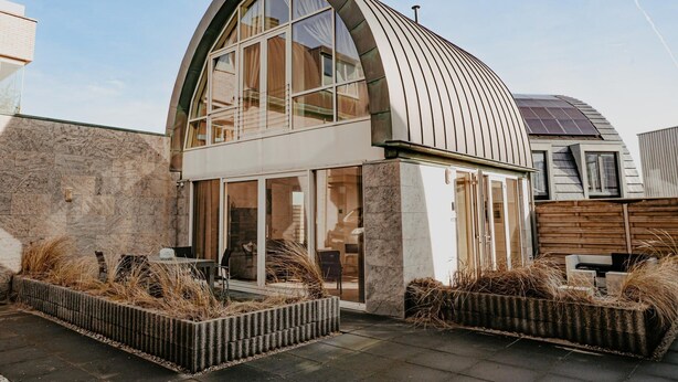 A modern house with a curved roof, large windows, and a solar panel on the roof. - Luxury Apartment Near the Beach (Egmond aan Zee)
