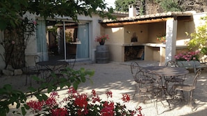 An outdoor patio with a table and chairs, a stone fireplace, and a garden with red flowers.