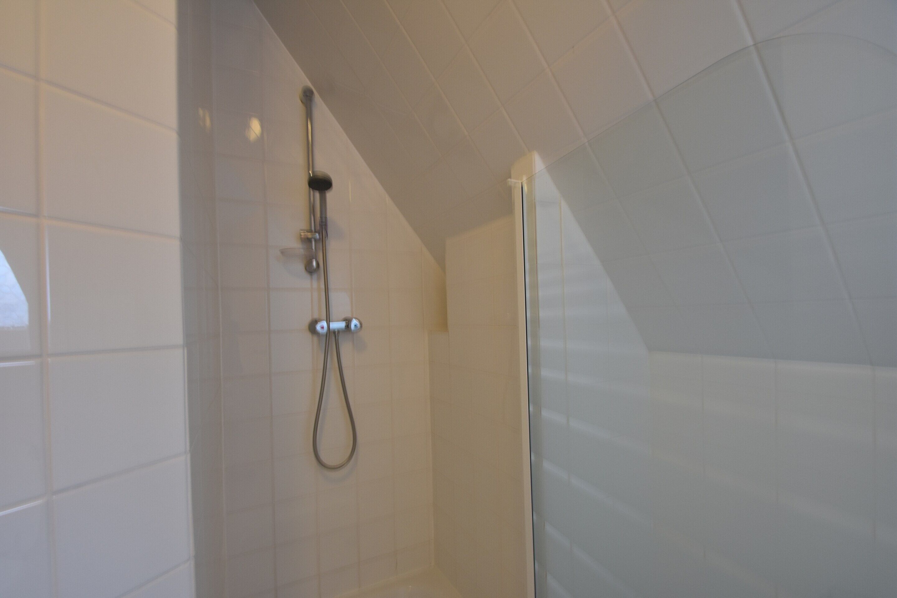 A shower with a glass door, tiled walls, and a handheld showerhead.