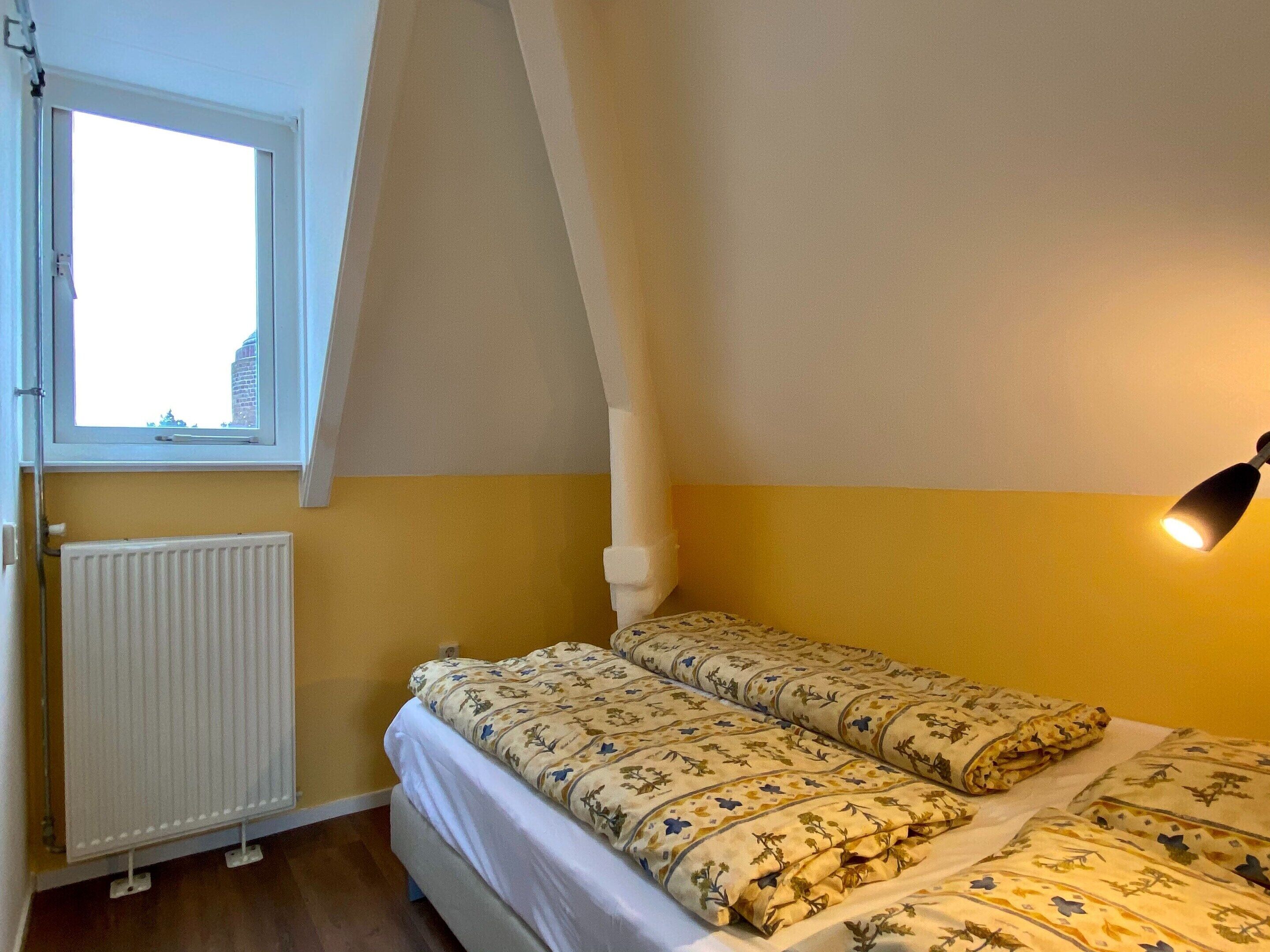 Un dormitorio con una cama, una ventana, un radiador y una lámpara.