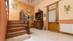 Un escalier en bois menant à un palier où se trouvent une horloge, un radiateur et une bibliothèque.