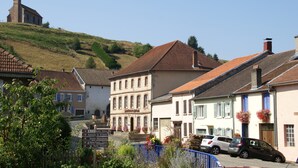 Un village européen traditionnel, avec des bâtiments historiques, une église située sur une colline et un ciel d’un bleu limpide.