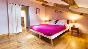 Une chambre avec un plafond en bois, un lit recouvert d’une couverture rose, deux lampes de chevet et une petite table de chevet.