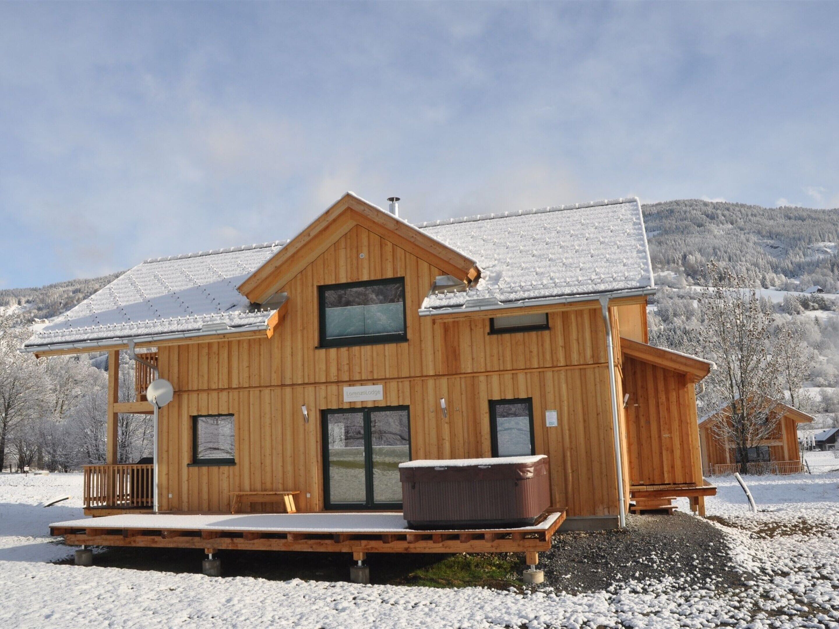 A wooden lodge with a covered porch, a large window, and a sign reading "Lomma Lodge."