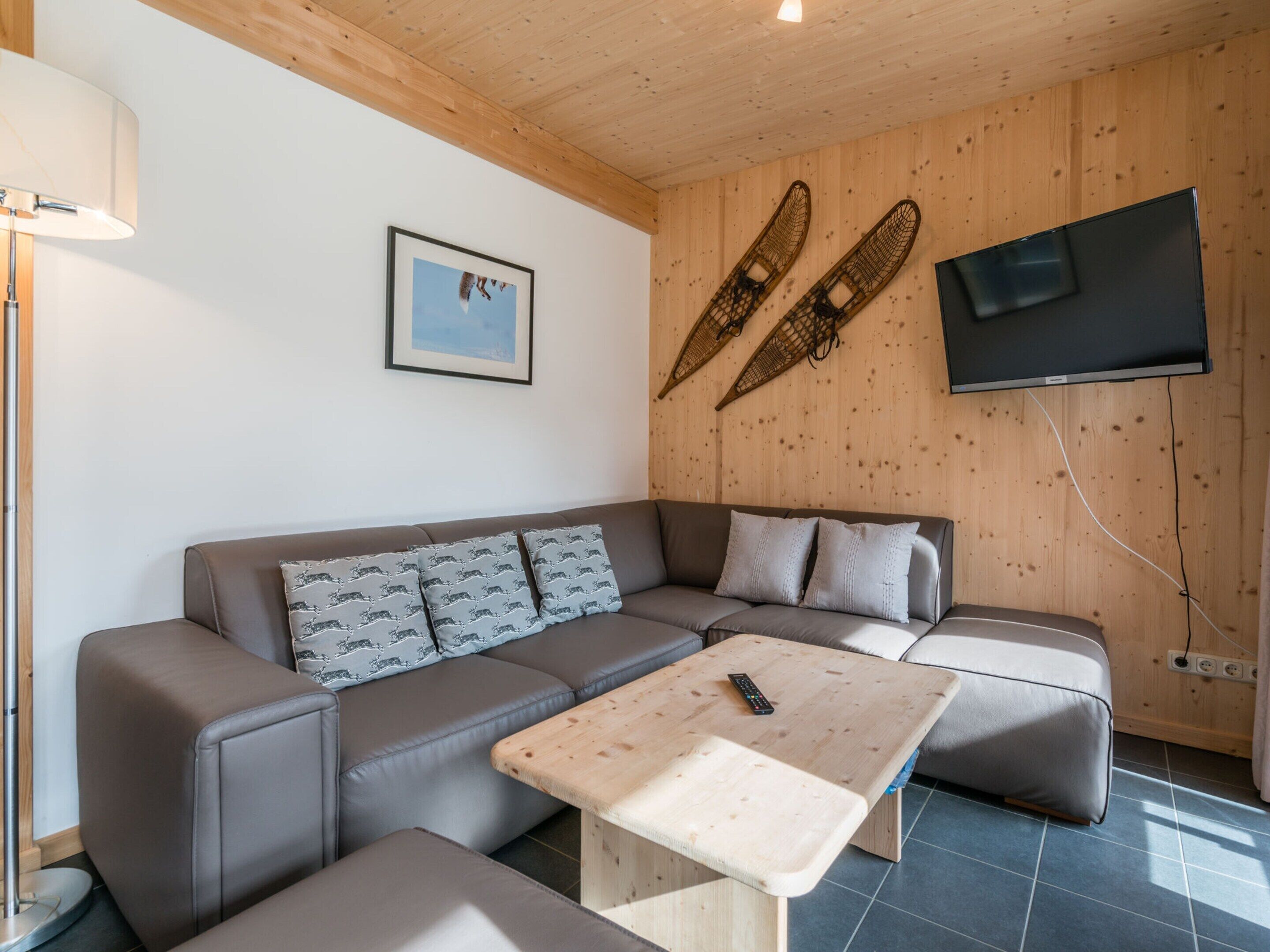 A modern living room with a sofa, a coffee table, and a TV mounted on a wooden wall.