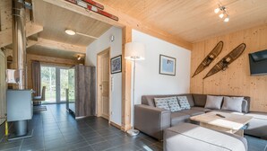 Ein modernes Wohnzimmer mit einer Couch, einem Hocker und einem Couchtisch. Es gibt einen Kamin, einen Fernseher und Holzwände.