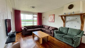 A living room with a sectional sofa, a green armchair, a wooden coffee table, and a television on a stand. - Holiday Home in Elsendorp With Garden (Elsendorp)