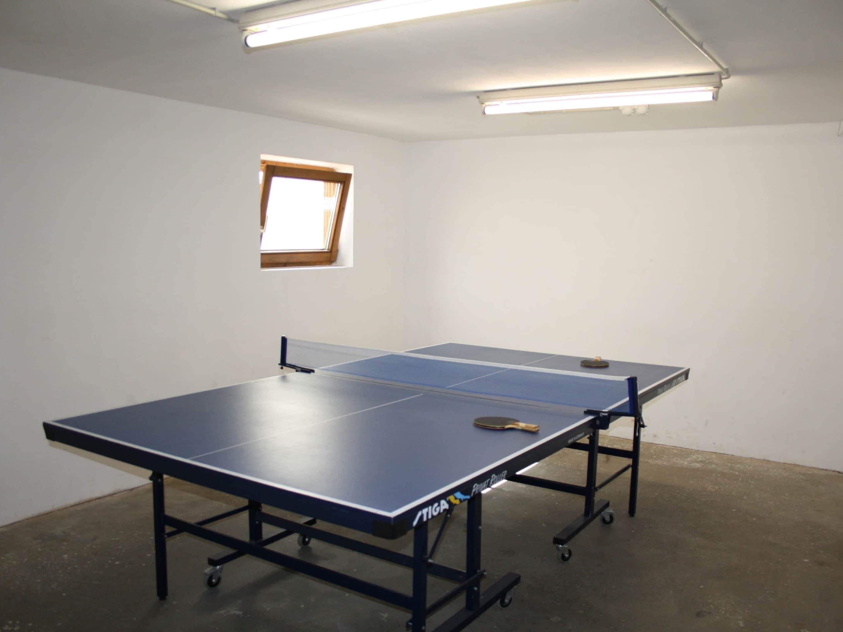 A ping pong table in a room with a small window and fluorescent lighting.