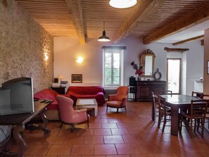 Ein gemütliches Wohnzimmer mit Fernseher, einer roten Couch und Sesseln, einem Essbereich mit Tisch und Stühlen sowie einer Küchenzeile mit Spiegel und Schränken.