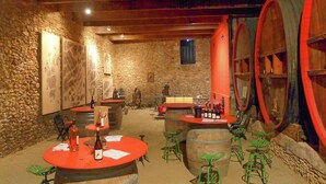 A rustic wine cellar with stone walls, wooden barrels, and green metal stools. - Holiday Home in Beziers With Pool and Vineyard (Murviel-les-Beziers)