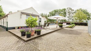 Ein Innenhof mit einem weißen Gebäude, Topfpflanzen, Gartenmöbeln und einem großen Sonnenschirm.