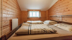 Una cabaña con dos camas, paredes de madera, una ventana con cortinas y un radiador.