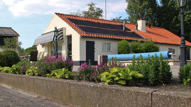 Ein Haus mit rotem Ziegeldach, Schornstein und einem Garten mit violetten Blumen.
