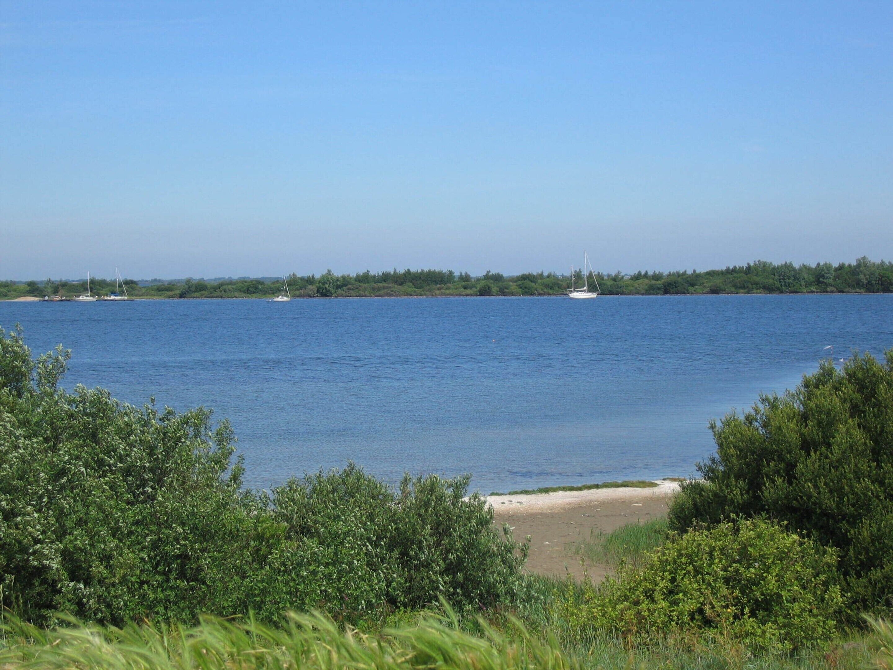 A calm body of water with boats, a sandy beach, and dense greenery.
