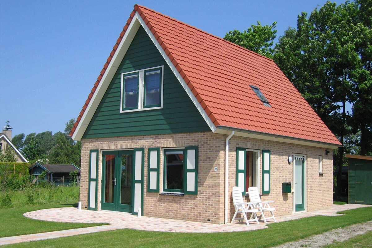A two-story house with a red-tiled roof and green siding. There are two windows on the second floor and two doors on the ground floor.
