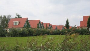 A row of houses with red roofs and green accents, surrounded by a grassy field and dense bushes. - Detached Holiday Home near Grevelingenmeer Lake (Zonnemaire)