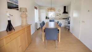 A modern kitchen with a dining area, featuring a wooden table, chairs, and a hanging light fixture. - Detached Holiday Home near Grevelingenmeer Lake (Zonnemaire)