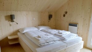 Quarto de cabana de madeira com duas camas, uma mesinha de cabeceira e um aquecedor fixado na parede.