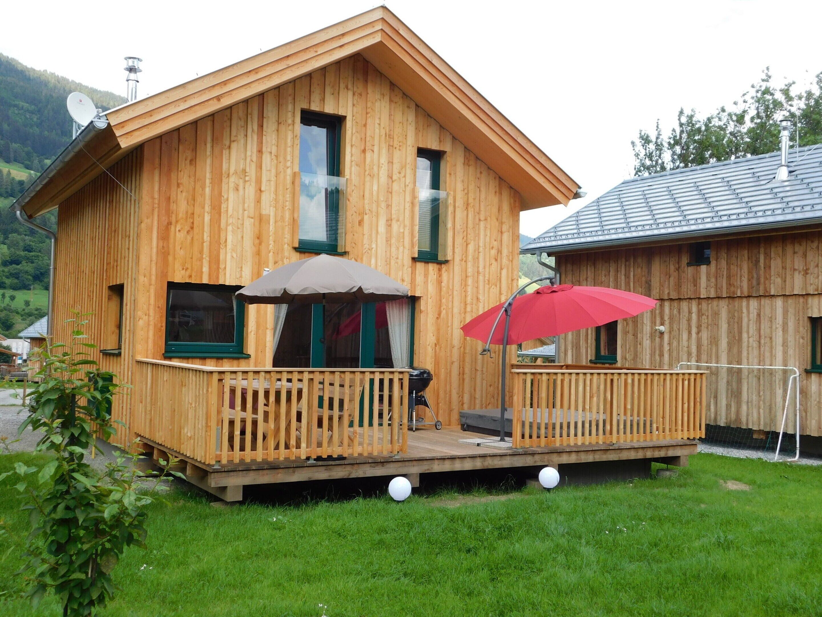 Une cabane en bois avec un balcon, un parasol rouge et une antenne parabolique.