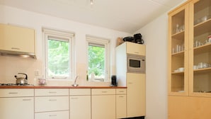 Cocina con armarios blancos, microondas, hervidor de agua y cafetera. Dos ventanas aportan luz natural.