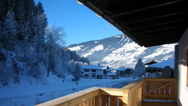 A wooden deck overlooking a snowy landscape with houses and mountains. - Boutique Apartment With Mountain View (Brixen im Thale)